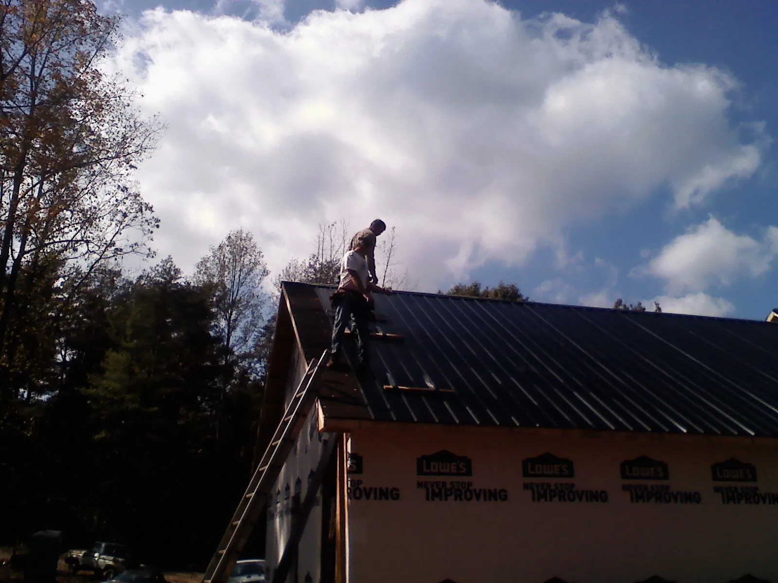 Roofer fastening dark metal panels high against a cloudy sky, from a Roof Inspection job in Watertown