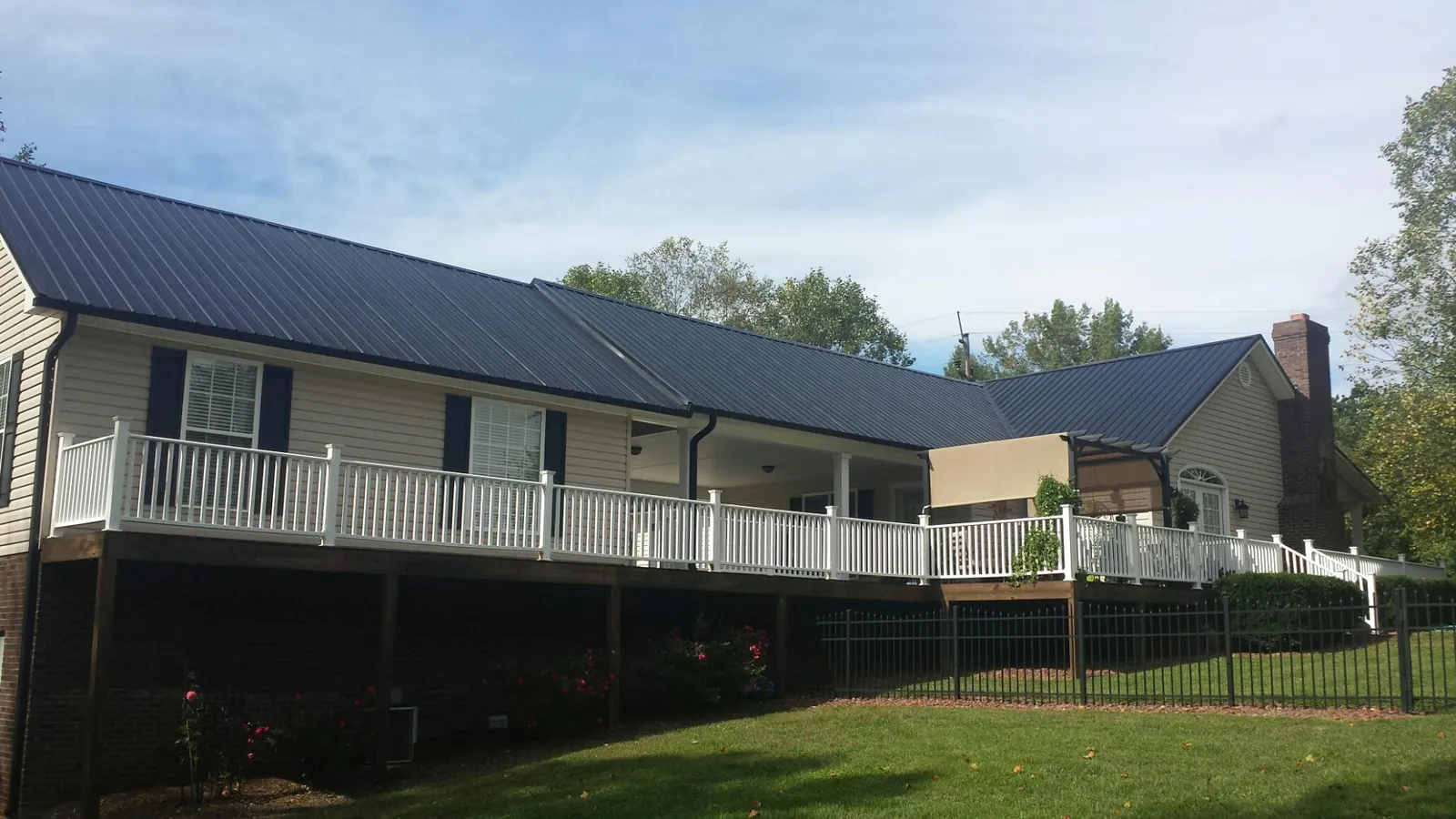 Black metal roof above a long white railed deck on a hillside home in Watertown
