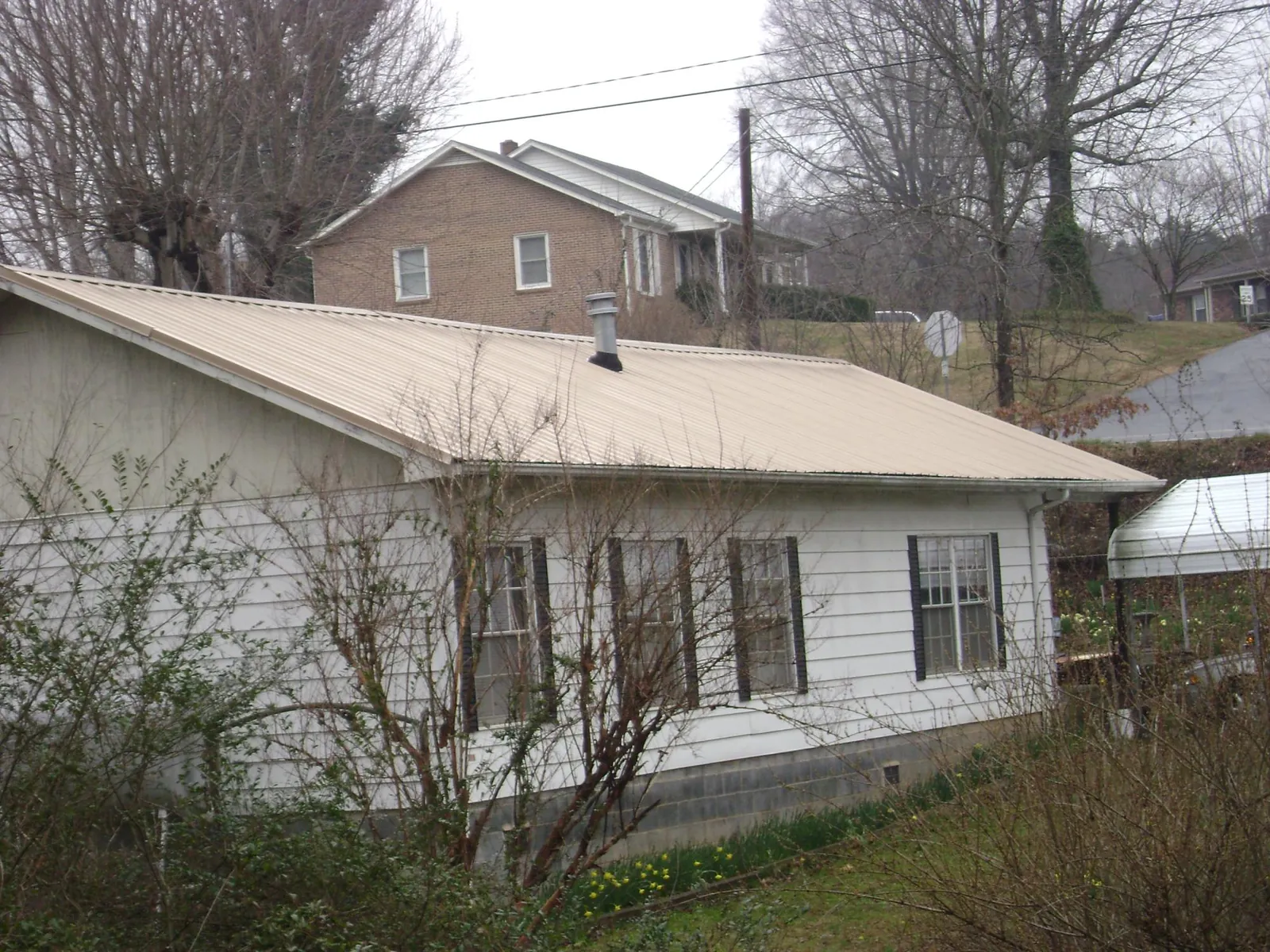 Tan metal roof on a white sided house set into a hillside — Commercial Roofing by Roofing Brothers in Watertown